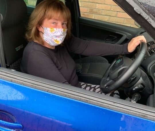 Woman wearing a mask at steering wheel of a car