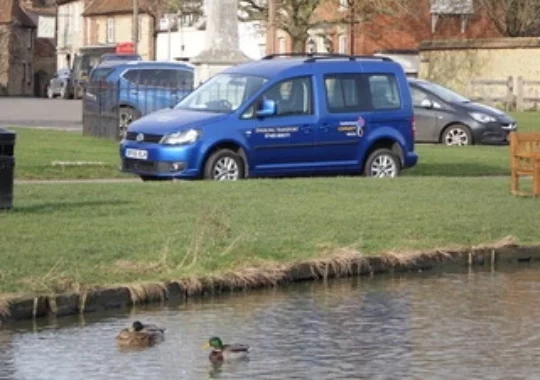 Blue car with Haddenham Community Vehicle signage on it, by Haddenham Village pond