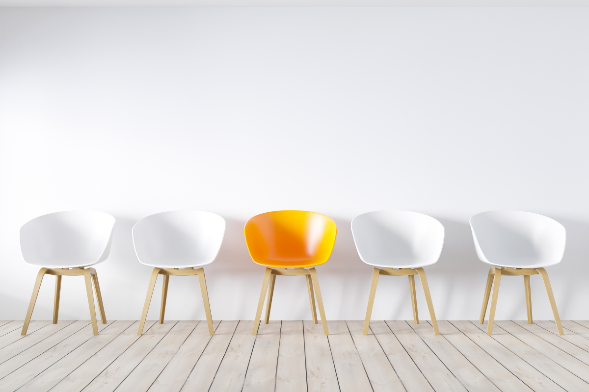 Image of five empty office chairs with the middle chair in yellow surrounded by white chairs